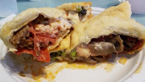 A close-up of a partially eaten stuffed burrito, revealing layers of meat, cheese, and vegetables inside a golden tortilla.