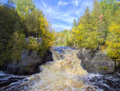 A cascading waterfall surrounded by vibrant autumn foliage and rocky cliffs under a blue sky.
