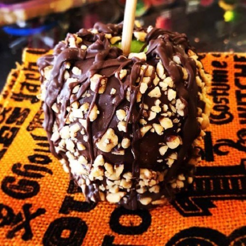 A chocolate-covered apple topped with chopped nuts, resting on an orange Halloween-themed napkin.