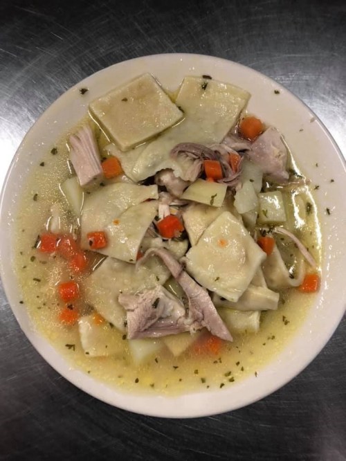 A bowl of soup with large dumplings, chicken pieces, carrots, and vegetables in a clear broth.