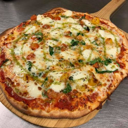 A freshly baked pizza topped with mozzarella, spinach, and colorful peppers on a wooden pizza peel.