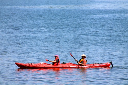 Two people in a red kayak paddling on a calm blue lake on a sunny day.