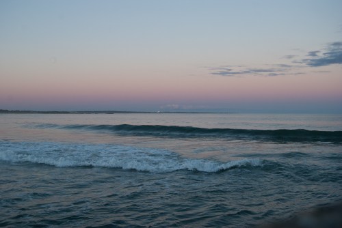 A serene ocean view at dusk, with gentle waves and a pastel sky transitioning from pink to blue.