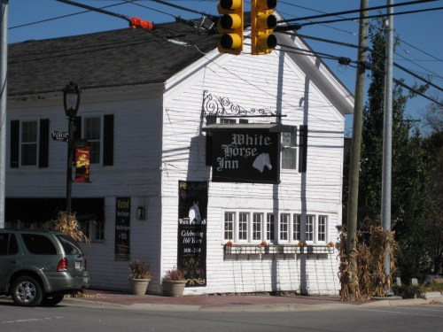 A white building with a sign reading "White Horse Inn," surrounded by autumn decorations and a traffic light.