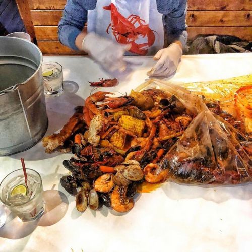 A table covered with a seafood boil, including shrimp, corn, and crab, alongside drinks in glasses.