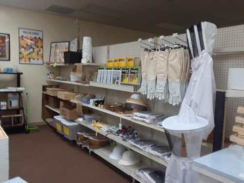 A well-organized store shelf displaying beekeeping supplies, including gloves, suits, and various tools.
