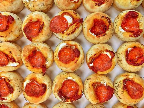 A close-up of golden-brown pizza bites topped with pepperoni and herbs, arranged in a neat grid pattern.