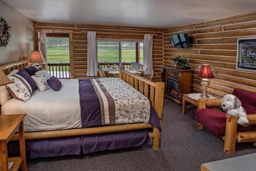 Cozy log cabin bedroom with a large bed, fireplace, and seating area, featuring scenic views through large windows.