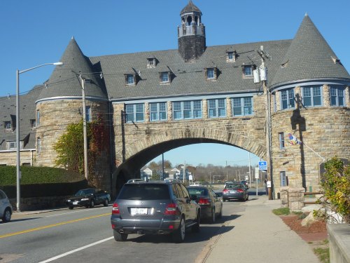 A stone archway building with a tower, flanked by cars on a road under a clear blue sky.