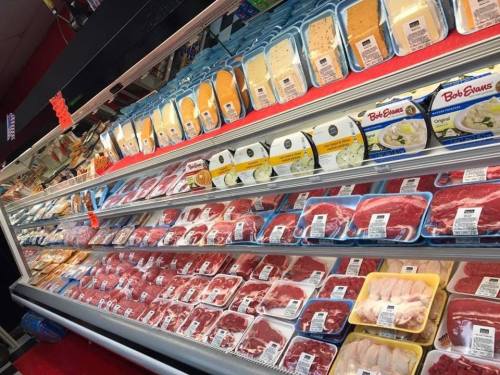 A refrigerated display case filled with various packaged meats and cheeses in a grocery store.