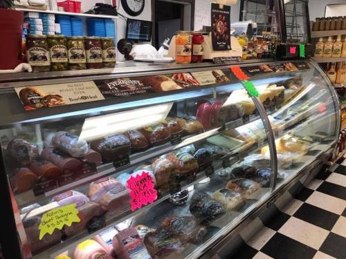 A deli display case filled with various meats, cheeses, and jars of condiments, with colorful price tags.