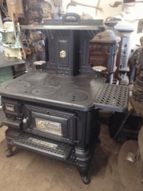 A vintage black cast iron stove with multiple burners and intricate detailing, set in a rustic environment.