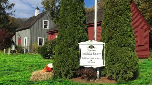 Sign for the Chatham Historical Society and Chestnut Hill School & Museum, surrounded by greenery and historic buildings.