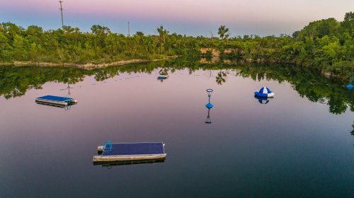 A serene lake at dusk with floating platforms and a buoy, surrounded by lush greenery and a calm reflection.