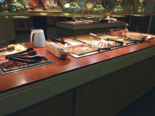 A buffet table with various food dishes, including meats and sides, under warm lighting.