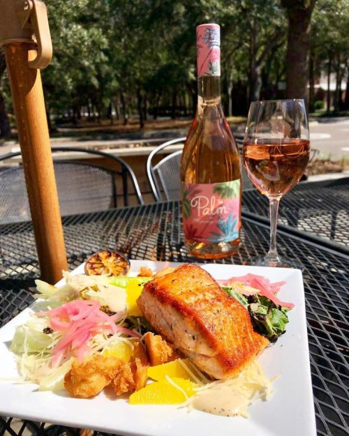 A plate of grilled salmon with salad, accompanied by a bottle of rosé wine and a glass, set outdoors on a table.