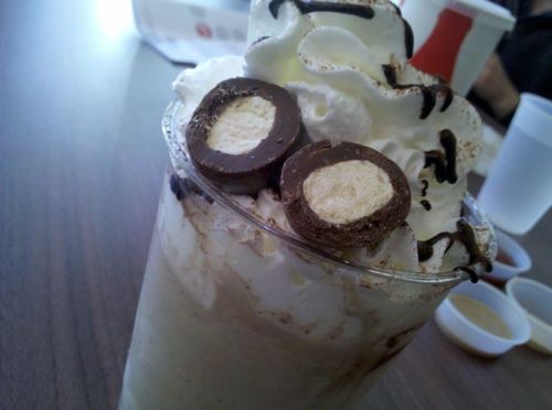 A creamy dessert topped with whipped cream, chocolate drizzle, and two chocolate-covered candies.