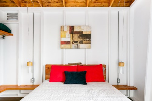 A cozy bedroom featuring a bed with red and black pillows, wooden accents, and a modern abstract painting on the wall.