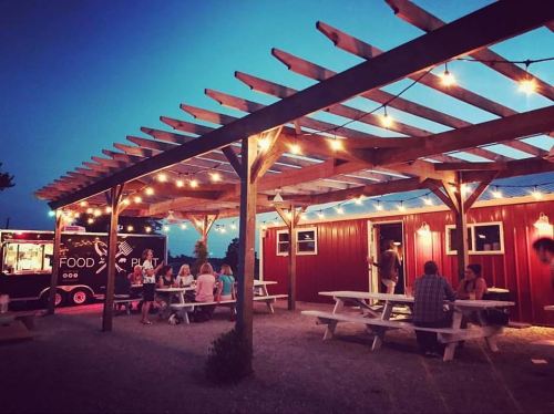 A food truck and outdoor seating area under string lights at dusk, with people enjoying the ambiance.