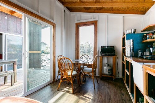 Cozy interior of a cabin with a dining table, kitchenette, and large windows letting in natural light.