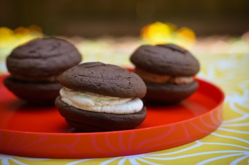 Three chocolate whoopie pies with creamy filling, arranged on a bright red plate against a colorful background.