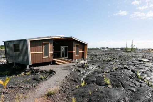 A modern house on a rocky lava landscape, surrounded by sparse vegetation and a clear blue sky.