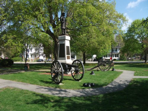 A park scene featuring a statue on a pedestal, surrounded by cannons and cannonballs, with trees and a pathway.