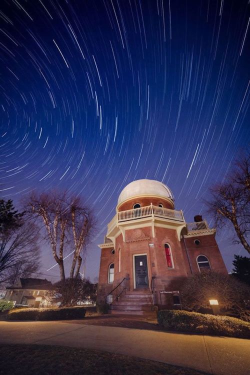 A historic observatory under a starry night sky, with star trails circling above and trees in the foreground.