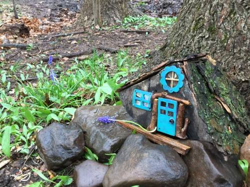 A small, whimsical fairy house made of wood and stones, nestled among green grass and flowers in a forest setting.