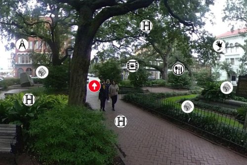 Two people walk along a tree-lined path in a park, with icons indicating nearby attractions and amenities.
