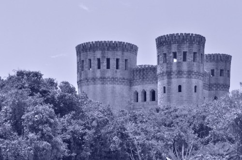 A medieval-style castle with tall towers, surrounded by lush greenery under a clear sky.