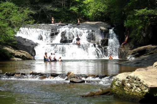 A scenic waterfall with people swimming and enjoying the water in a lush, green forest setting.