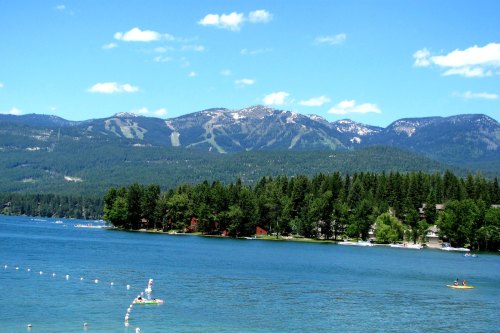 A serene lake surrounded by lush trees and mountains under a clear blue sky, with people enjoying water activities.