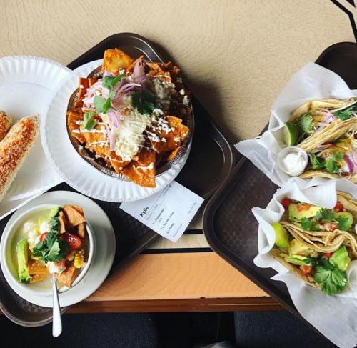 A spread of Mexican dishes including nachos, tacos, and a bowl of fruit, served on trays with garnishes.
