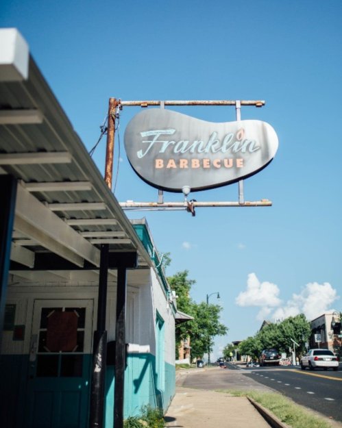 Sign for Franklin Barbecue against a clear blue sky, with a street view and buildings in the background.