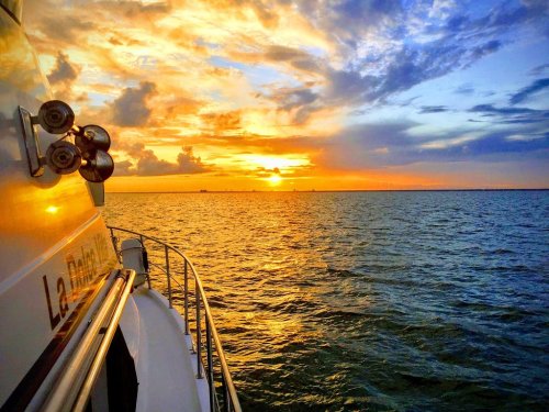 A vibrant sunset over the water, with colorful clouds and a boat's side in the foreground.