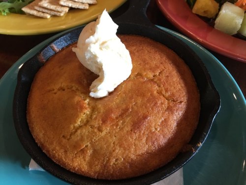 A golden cornbread in a cast iron skillet, topped with a dollop of butter, served with crackers and a colorful salad.