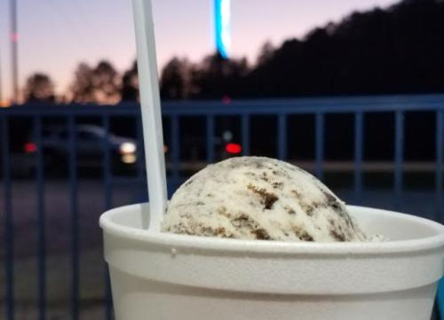 A close-up of a cup of ice cream with a spoon, set against a blurred sunset background.