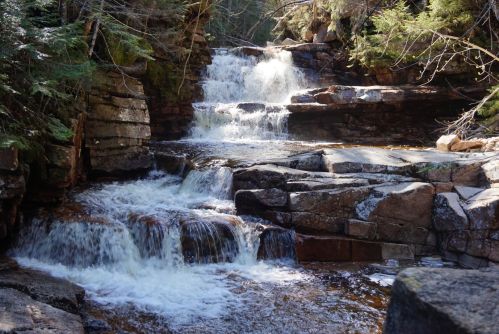 A serene waterfall cascading over rocky terrain, surrounded by lush greenery and sunlight filtering through the trees.