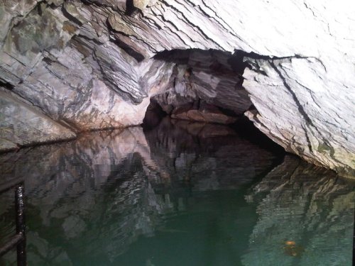 A dark cave entrance with rocky walls, reflecting in still water below.