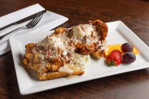 A plate of fried chicken topped with creamy gravy on toast, garnished with strawberries, grapes, and an orange slice.