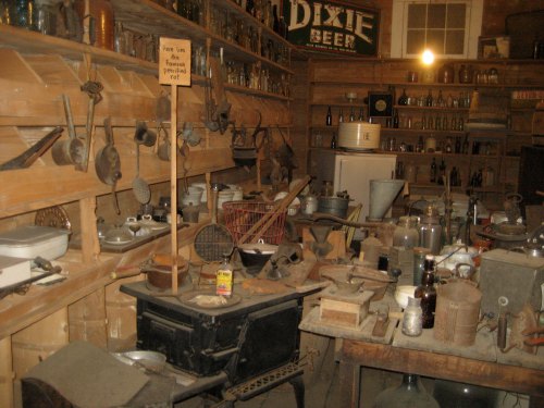 A cluttered vintage store filled with various old tools, kitchenware, and bottles on wooden shelves.