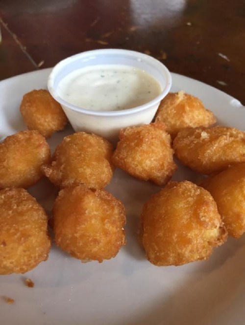 A plate of golden, crispy cheese balls served with a small cup of ranch dressing.
