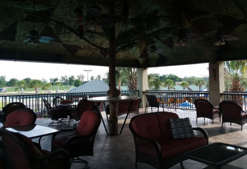 A shaded outdoor seating area with wicker chairs and tables, surrounded by greenery and a view of the landscape.