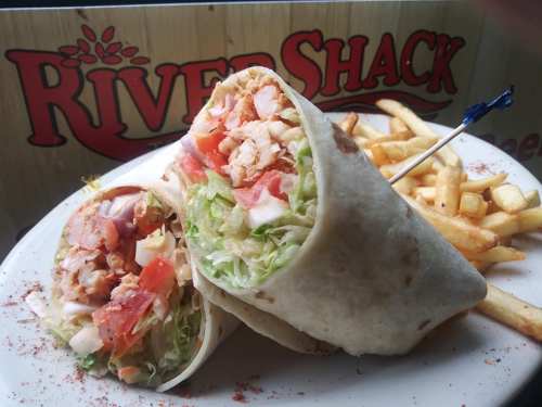 A close-up of a chicken wrap filled with lettuce, tomatoes, and cheese, served with fries on a plate.