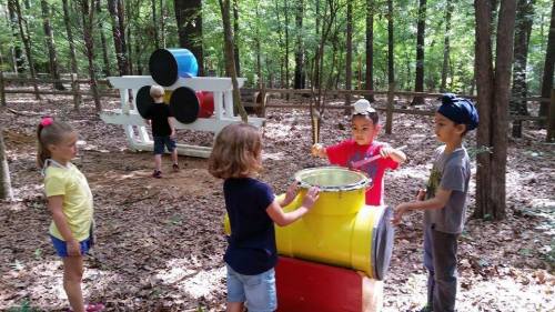 Children playing with colorful outdoor equipment in a wooded area, engaging in imaginative activities.