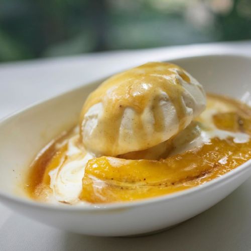 A dish featuring a scoop of ice cream topped with caramel sauce and slices of cooked banana in a white bowl.