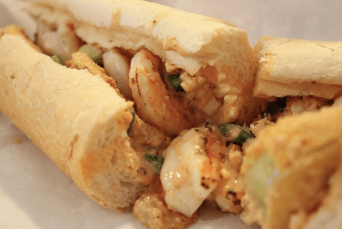 Close-up of a shrimp sandwich filled with shrimp, spices, and vegetables, served in a crusty bread roll.