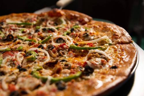 A close-up of a pizza topped with onions, green peppers, olives, and various meats on a golden crust.