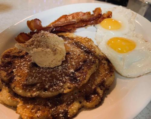 A plate of pancakes topped with butter, served with crispy bacon and two sunny-side-up eggs.